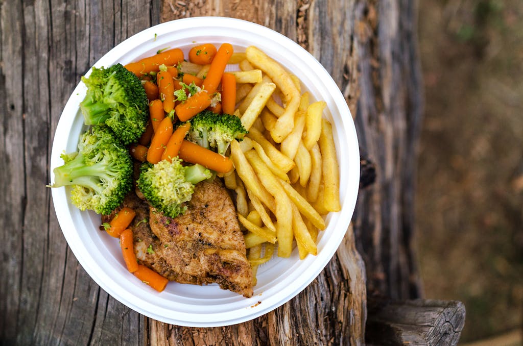 A delicious plate of chicken, fries, and fresh vegetables served on a rustic wooden table, ideal for a healthy meal.