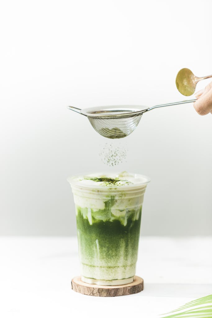 Delicious green matcha latte with milk froth in a clear disposable cup, styled with matcha powder.