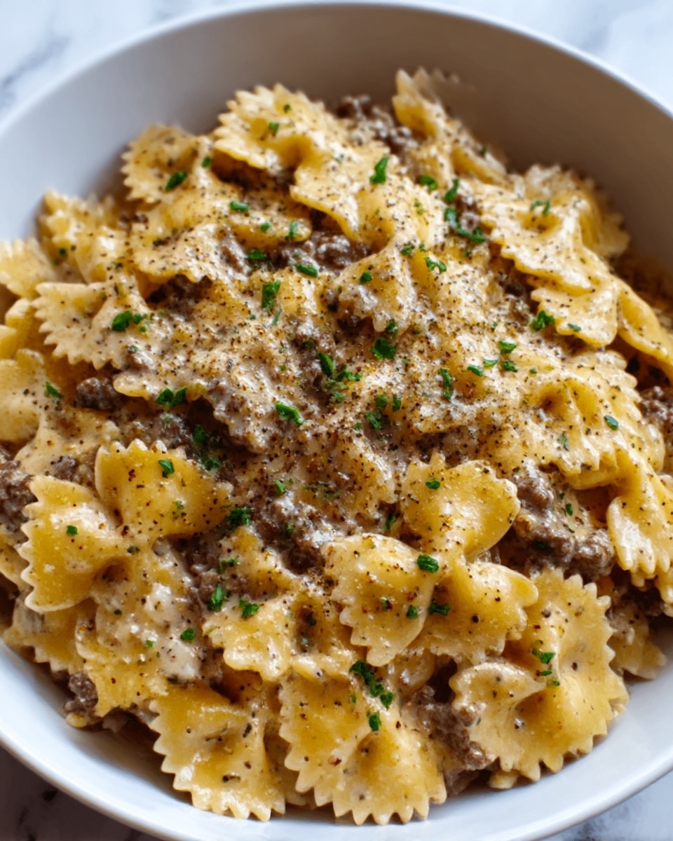 A white bowl filled with farfalle pasta in a creamy sauce. The pasta is light yellow with a smooth texture, mixed with small pieces of browned ground beef scattered evenly on top and throughout the dish. There is a light sprinkling of finely chopped green herbs and ground black pepper spread over the pasta, adding contrast and detail. The bowl sits on a white marbled surface. Photo taken with an iphone --ar 4:5 --v 7