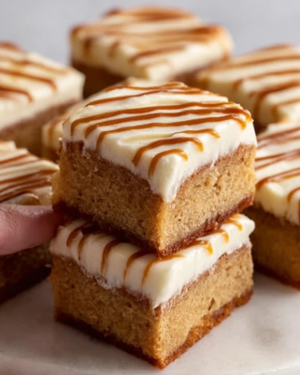 The image shows several square cake pieces stacked closely, each with two main layers. The bottom layer is a light brown, dense cake with a smooth texture. The top layer is creamy white frosting, thickly spread, with thin caramel-colored lines drizzled evenly across the surface. One piece is held by a woman’s hand above the rest, emphasizing the neat layers and smooth frosting. The cake pieces are placed on a white marbled surface. Photo taken with an iphone --ar 4:5 --v 7