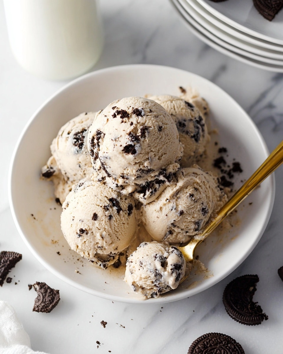 The image shows four scoops of light beige ice cream with dark chocolate cookie pieces mixed in, placed closely together in the center of a white plate. The ice cream scoop texture is creamy with visible black cookie bits throughout each scoop. A gold spoon is on the right side of the plate, holding a small scoop of the ice cream. Around the plate, there are broken chocolate sandwich cookie pieces scattered on a white marbled surface. In the background, slightly out of focus, there is a white bottle and a stack of white plates. photo taken with an iphone --ar 4:5 --v 7