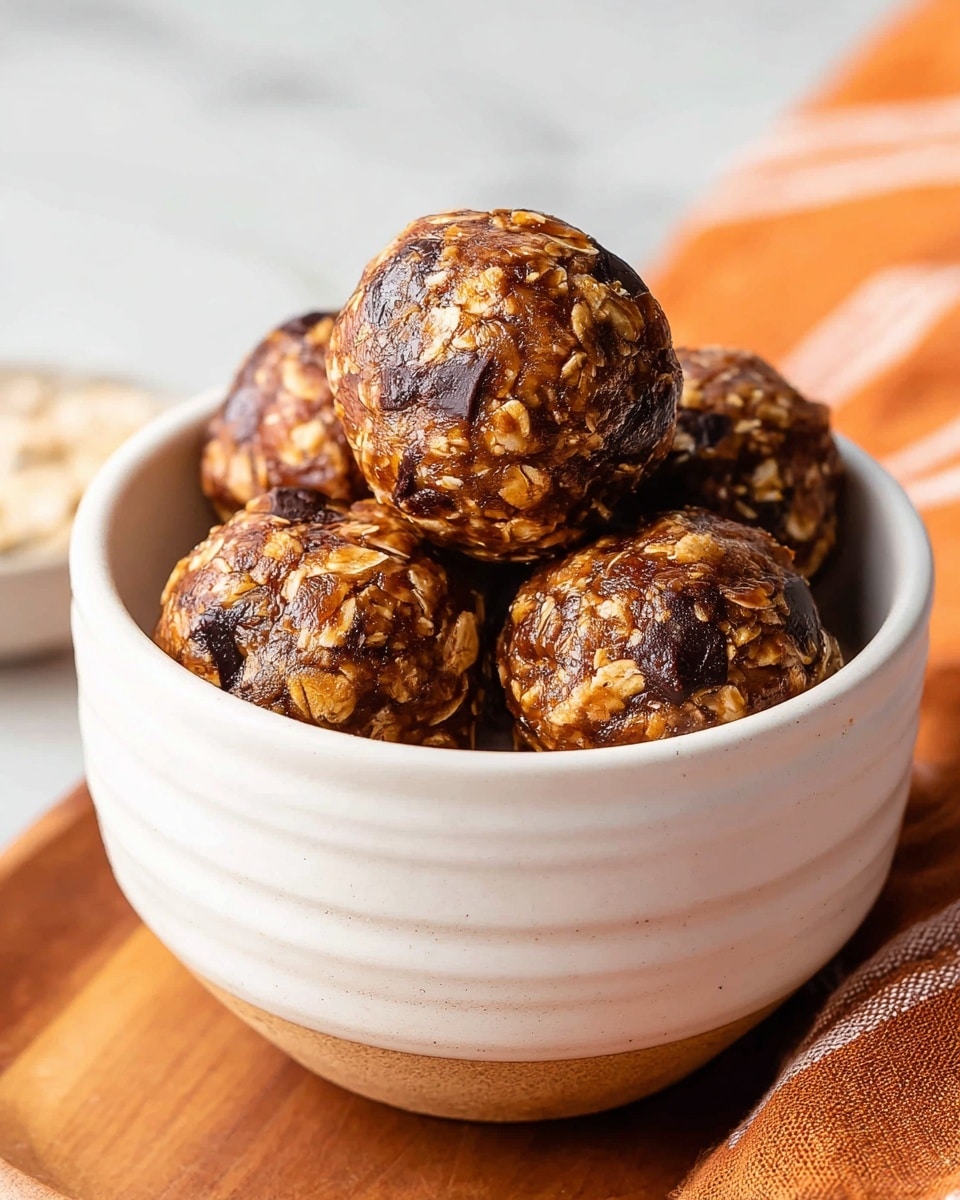 A close-up of a white ribbed bowl filled with five round energy balls, stacked with three on the bottom layer and two on top. The energy balls have a textured surface showing oats and dark brown chocolate chunks, with a glossy coating that gives them a slightly sticky look. The bowl sits on a wooden board, next to an orange-striped cloth on a white marbled surface. The lighting softly highlights the textures and colors of the balls. photo taken with an iphone --ar 4:5 --v 7