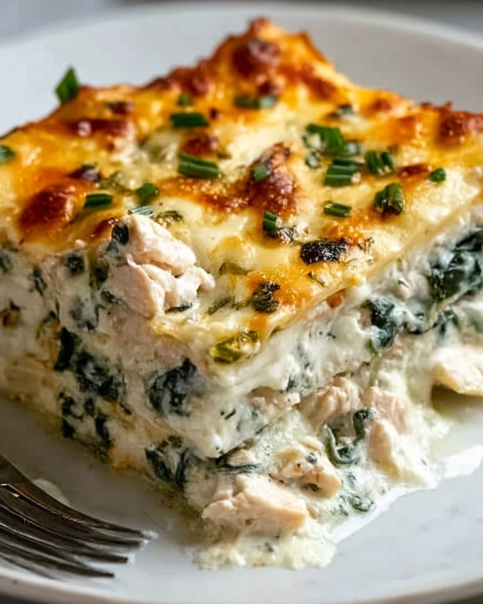 A close-up of a slice of baked lasagna on a white plate, showing multiple layers of creamy white sauce mixed with green spinach leaves, chunks of white chicken, and a golden brown melted cheese topping with bubbly texture. The edges of the cheese appear slightly crispy and browned, with herbs sprinkled on top for added detail. The white marbled surface is visible under the plate, adding brightness to the scene. photo taken with an iphone --ar 4:5 --v 7