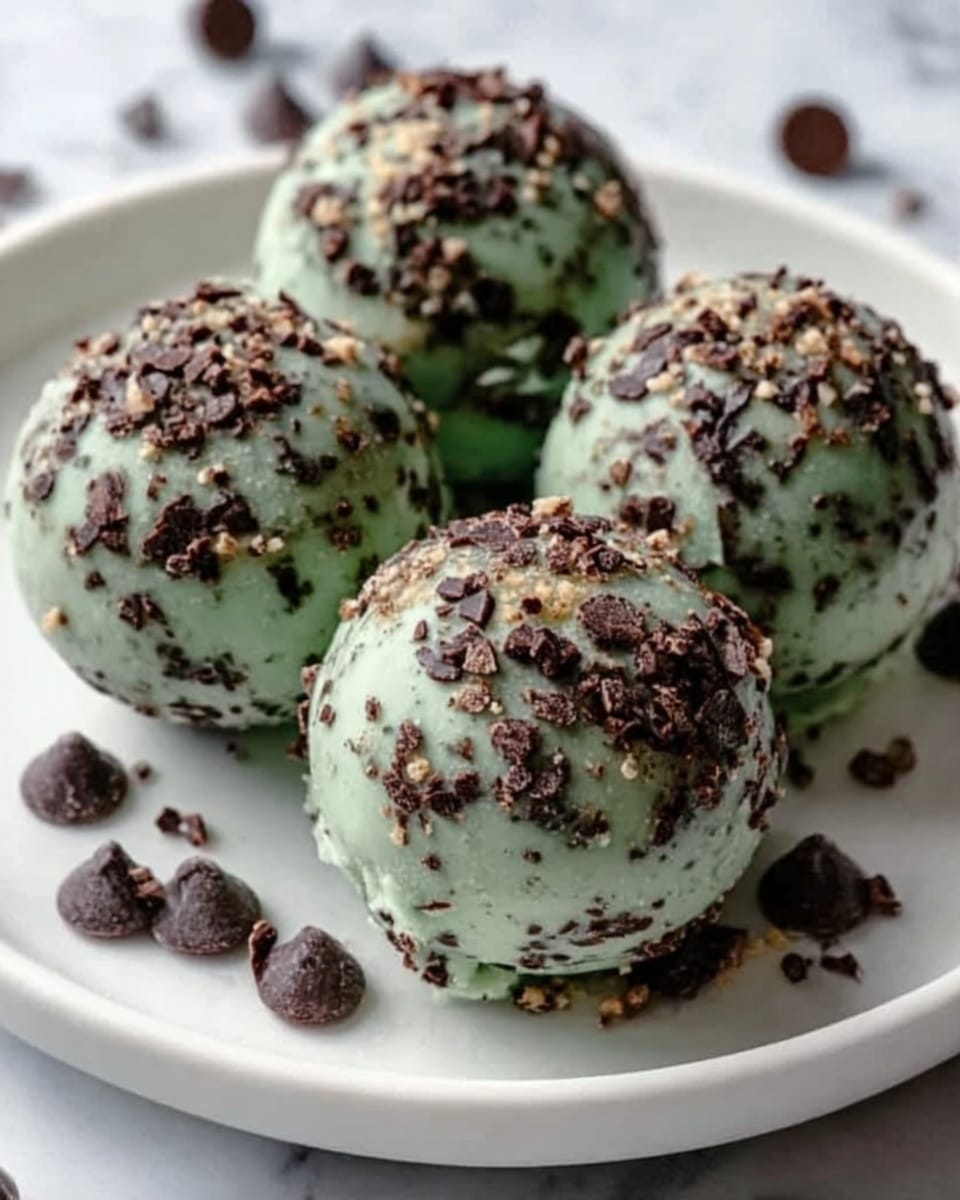 Five round mint green ice cream balls covered with small dark chocolate chunks and tiny light brown pieces, arranged on a white plate with a few dark chocolate chips scattered around. The ice cream balls have a smooth texture with uneven chocolate toppings, creating a mix of green, dark brown, and light brown colors. The scene is set on a white marbled surface. Photo taken with an iphone --ar 4:5 --v 7
