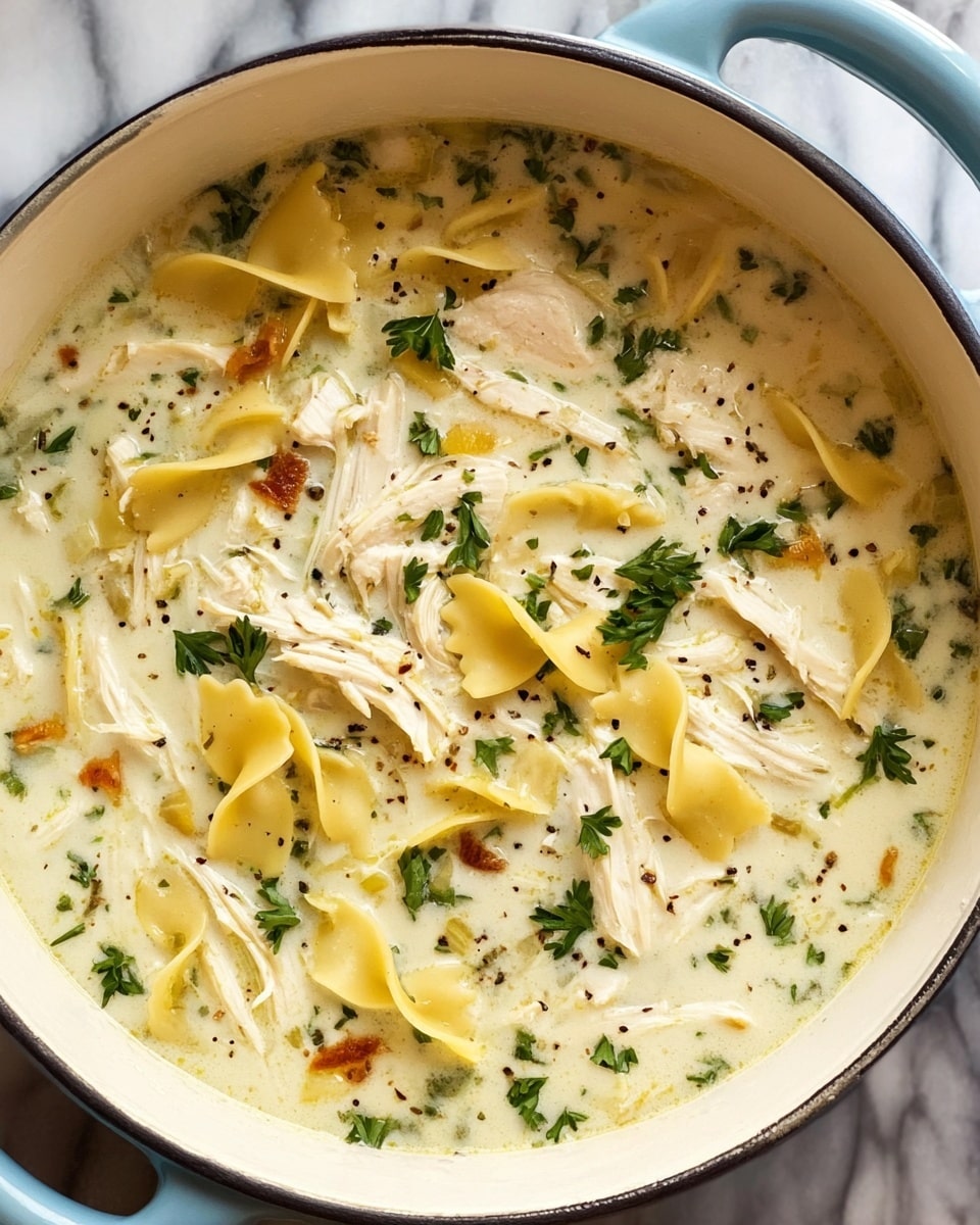 A close-up view of a creamy chicken noodle soup in a light blue pot with white inside, placed on a white marbled surface. The soup has at least three visible layers: the base layer is a light creamy broth with a smooth texture, scattered with very small black pepper bits. Floating on top are shredded white chicken pieces and yellowish flat pasta pieces with ruffled edges. Green parsley leaves are spread over the soup, adding color contrast. Some small orange-brown bits are also seen mixed in the broth. The pot handle is visible on the right side. Photo taken with an iphone --ar 4:5 --v 7