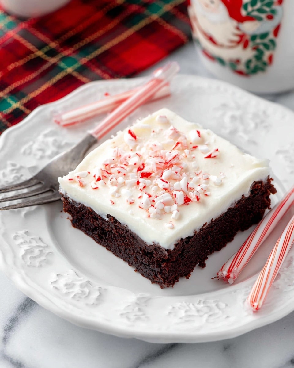 A single square piece of dessert is shown with two clear layers: a thick, rich dark brown brownie base on the bottom, and a smooth, thick layer of white frosting on top. The frosting is sprinkled with small, broken bits of red and white peppermint candy. The dessert sits on a white plate with delicate embossed edges and cut-out patterns, placed on a white marbled surface. Two red-and-white striped candy canes lay casually behind the plate, and part of a silver fork hangs off the side of the plate. A red, green, and gold plaid cloth and a ceramic Santa mug are partially visible in the background. photo taken with an iphone --ar 4:5 --v 7