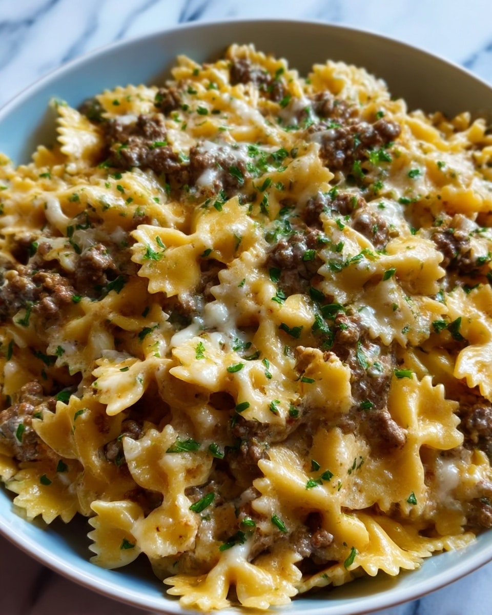 The image shows a close-up view of a pasta dish with bowtie-shaped pasta mixed with pieces of browned ground meat. The pasta is coated in a creamy sauce with a slightly golden top layer, sprinkled with small green herb bits for a fresh look. The texture is soft and slightly cheesy with visible seasoning dots. The food fills a white plate that sits on a white marbled surface. Photo taken with an iphone --ar 4:5 --v 7