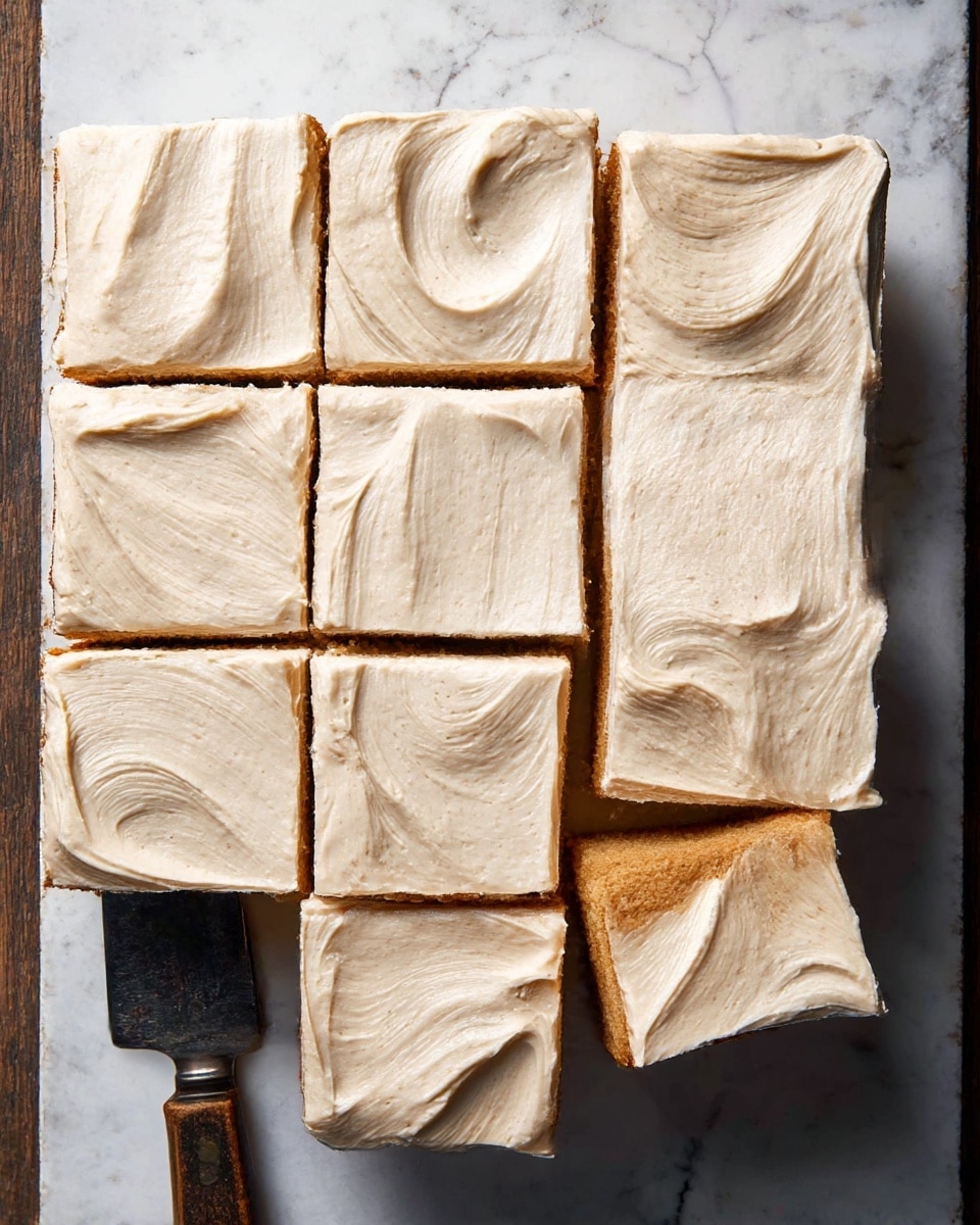 The image shows a square cake cut into nine pieces and topped with a thick, creamy layer of light beige frosting that has smooth, visible swirls on the surface. The cake base beneath the frosting has a warm, golden-brown color and appears soft and moist. The pieces are placed closely together on a white marbled textured surface, with a piece slightly separated from the rest at the bottom right. A vintage-style knife with a dark handle is partially visible on the left side. Photo taken with an iphone --ar 4:5 --v 7